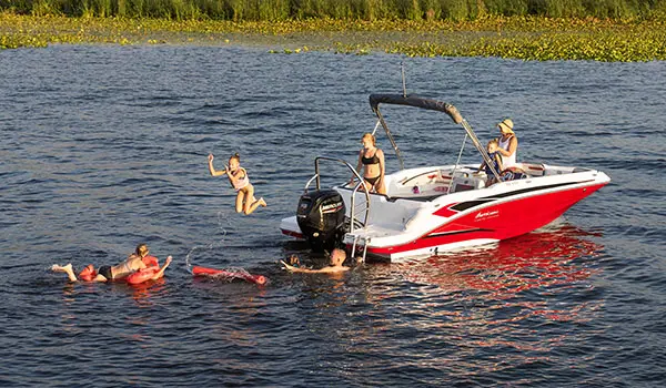 Family playing in the lake near the stern of a Hurricane SunDeck Sport 205 OB deck boat.