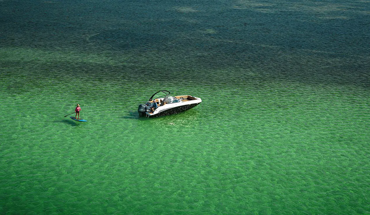 person paddle boarding behind a hurricane sundeck ob boat