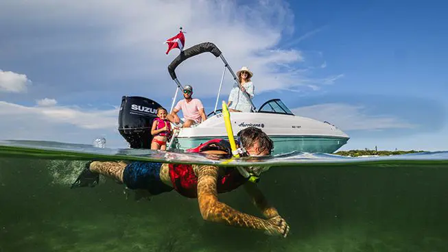 Kid snorkeling in the ocean while his family watches on a Hurricane deck boat.