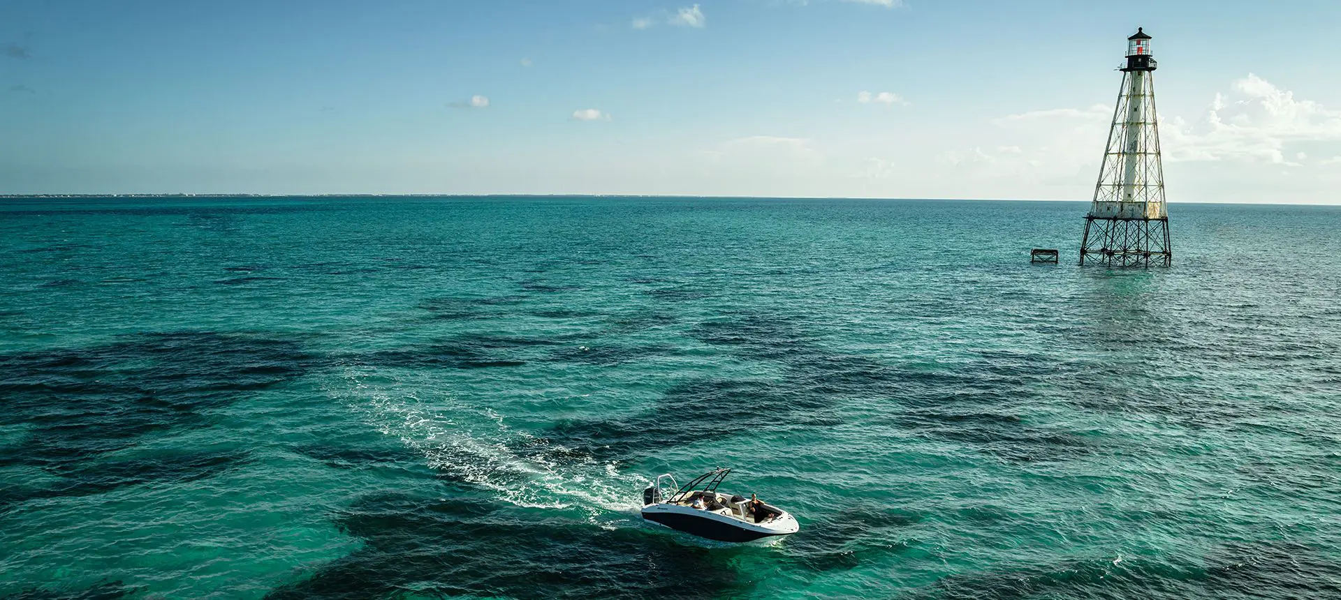 Aerial view of a Hurricane deck boat cruising by a lighthouse.