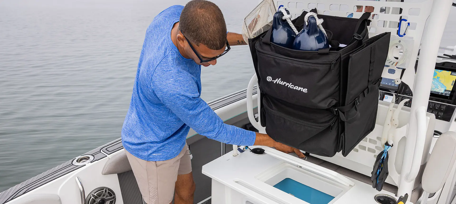 A man grabbing some gear from a storage area of a Hurricane Center Console fishing deck boat.