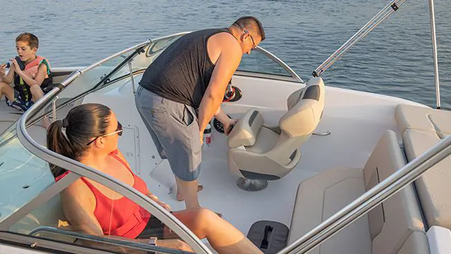 A man adjusting the captain's seat on a Hurricane 187 IO deck boat.