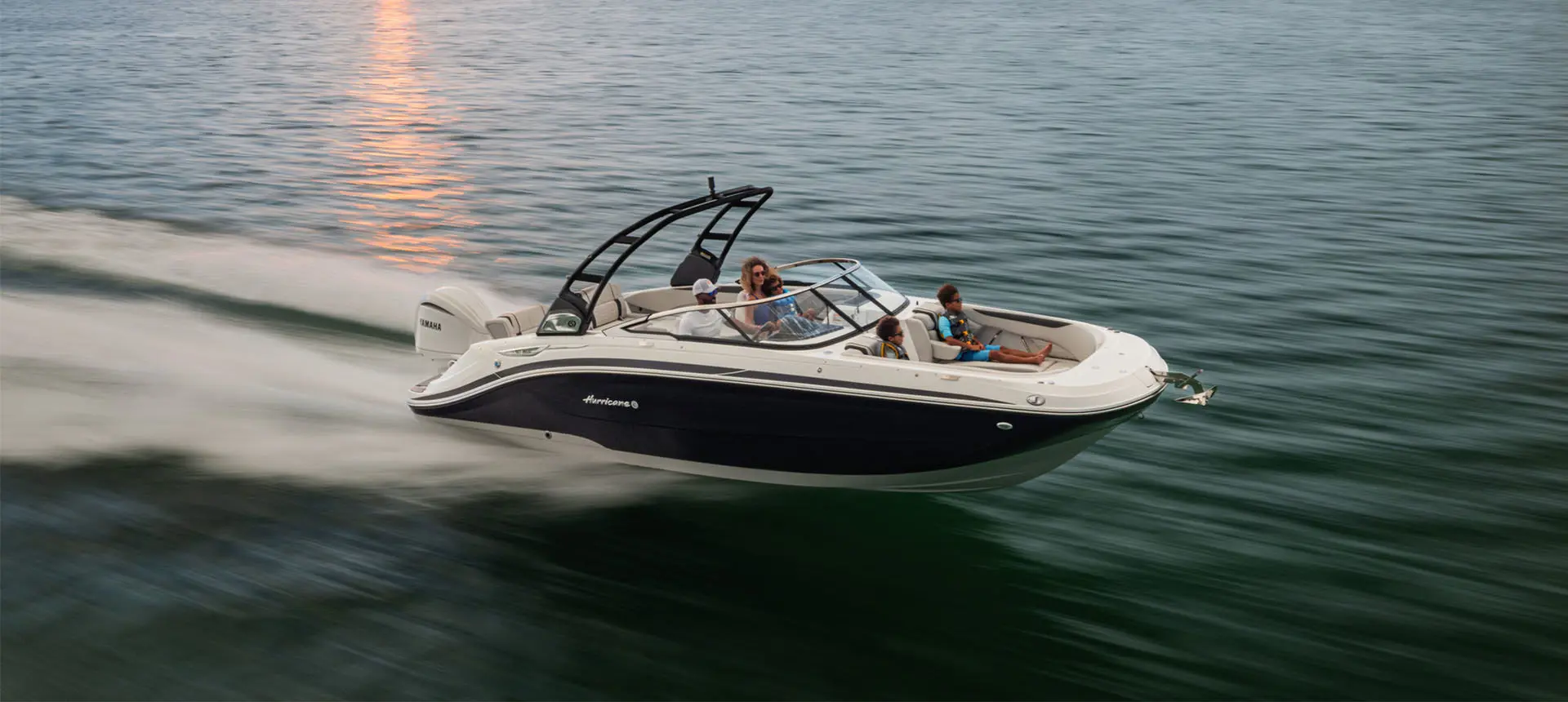 Hurricane Sundeck 2600 OB deck boat cruising on the ocean at sunset.