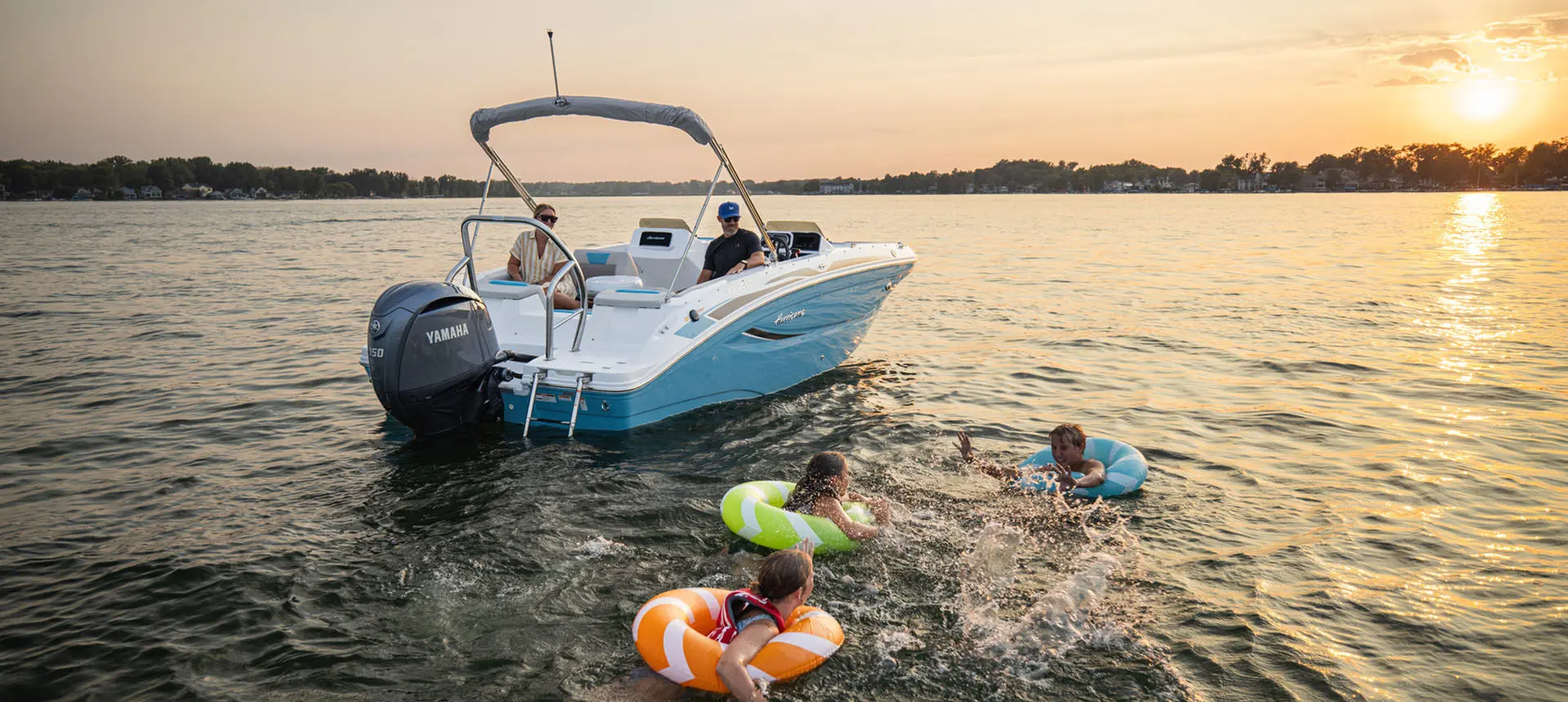 Kids playing in lake in floaty toys near a parked Hurricane Sundeck Sport 2050 OB.