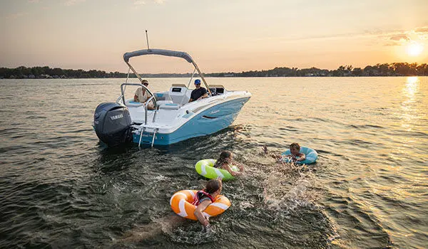 Kids playing in lake in floaty toys near a parked Hurricane Sundeck Sport 2050 OB.