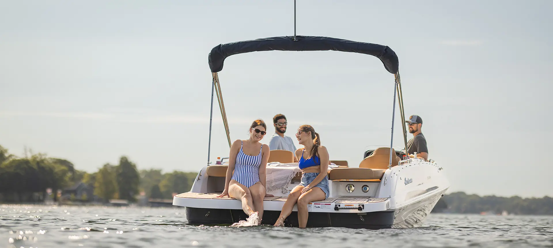2 women sitting on the stern swim platform on a Hurricane SunDeck Sport I/O deck boat.