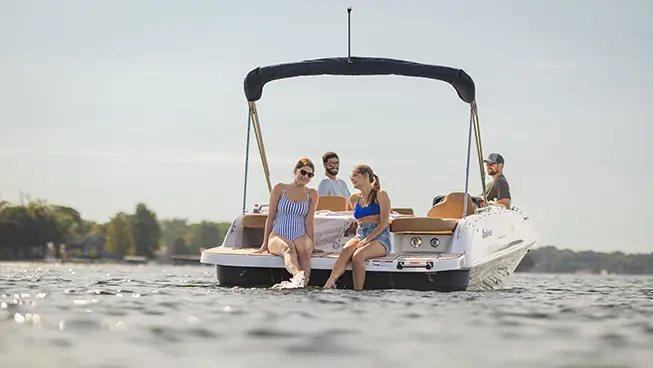 2 women sitting on the stern swim platform on a Hurricane SunDeck Sport I/O deck boat.