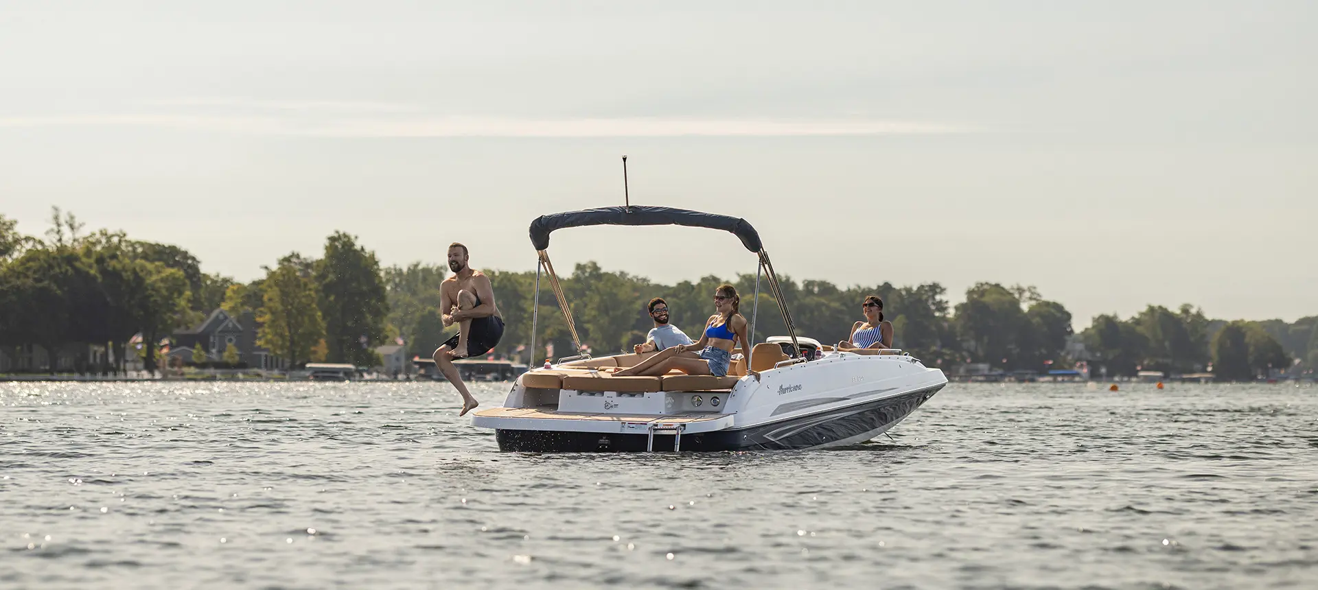 Man jumping off the swim platform while his friends watch on a Hurricane SunDeck Sport I/O deck boat.