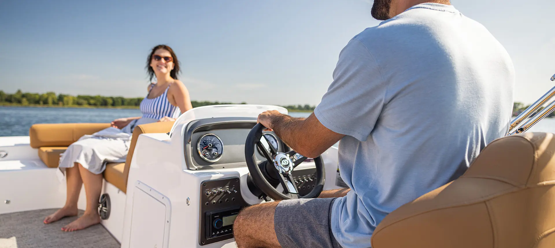 Closeup of a man sitting at the captain's helm on a Hurricane SunDeck Sport I/O deck boat.