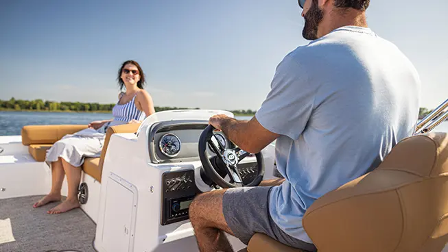 Closeup of a man sitting at the captain's helm on a Hurricane SunDeck Sport I/O deck boat.