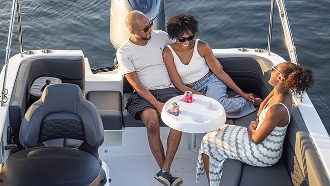Family of 3 chatting around the stern table on their Hurricane SunDeck Sport OB deck boat.