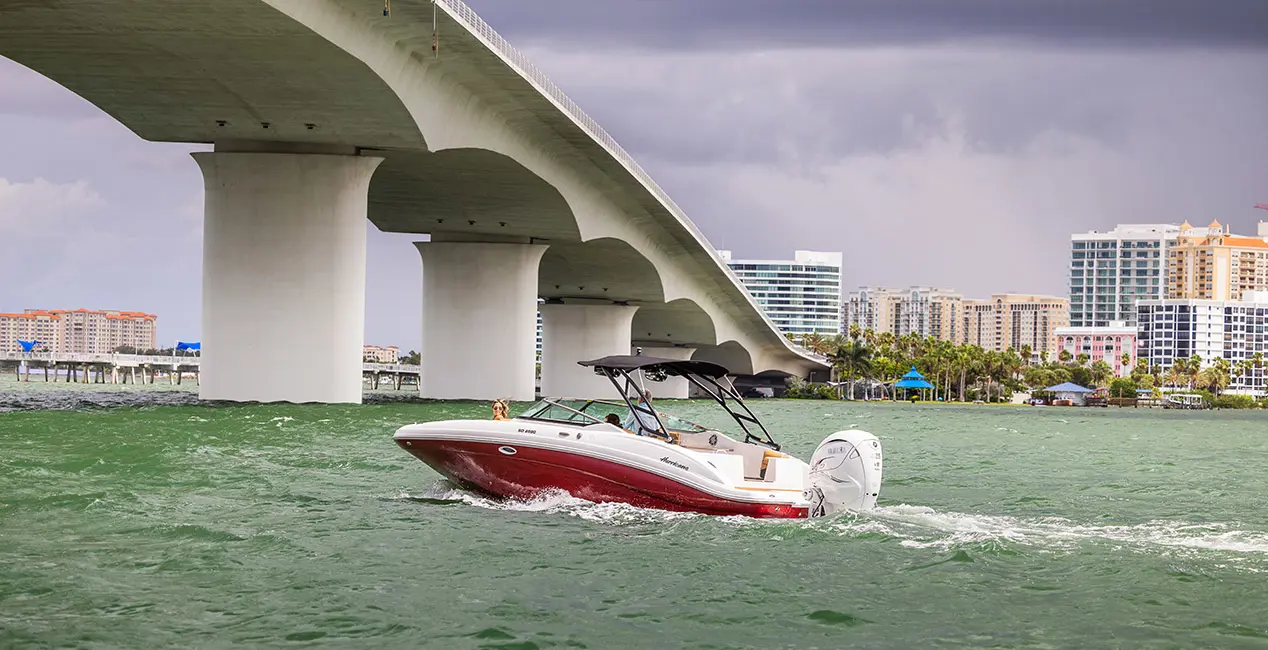 Side profile of a Hurricane yacht certified deck boat cruising on the ocean going under a bridge.