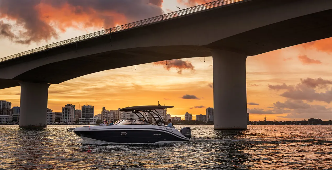 Side profile of a Hurricane yacht certified deck boat cruising under a bridge on the ocean.