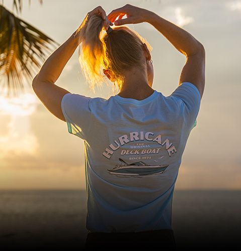 Woman tying ponytail during sunset while wearing light blue Hurricane Deck Boat t-shirt. 