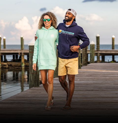 Man and woman walking on dock smiling while wearing Hurricane sweatshirts. 