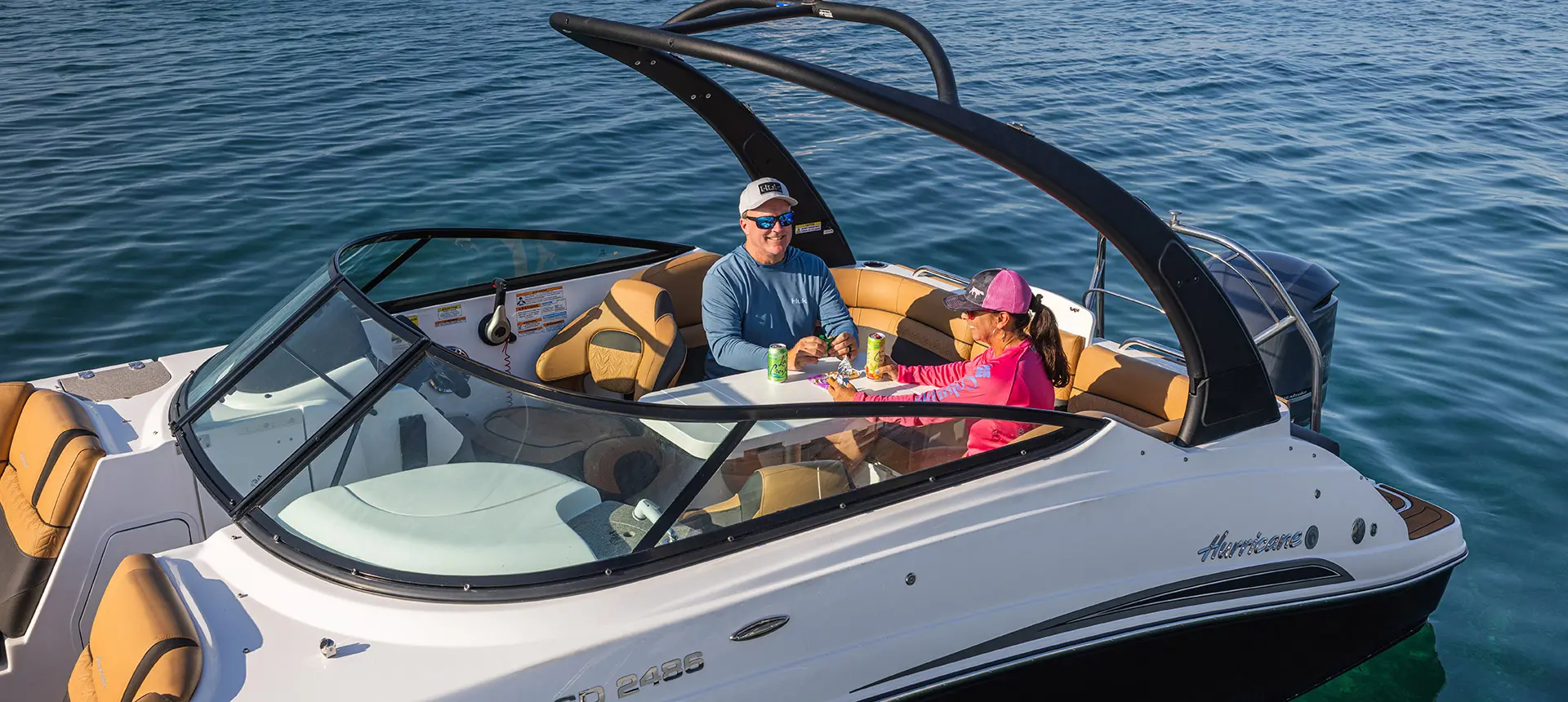 Side/aerial view of a couple having a snack on the stern table on a Hurricane Entertainment deck boat.
