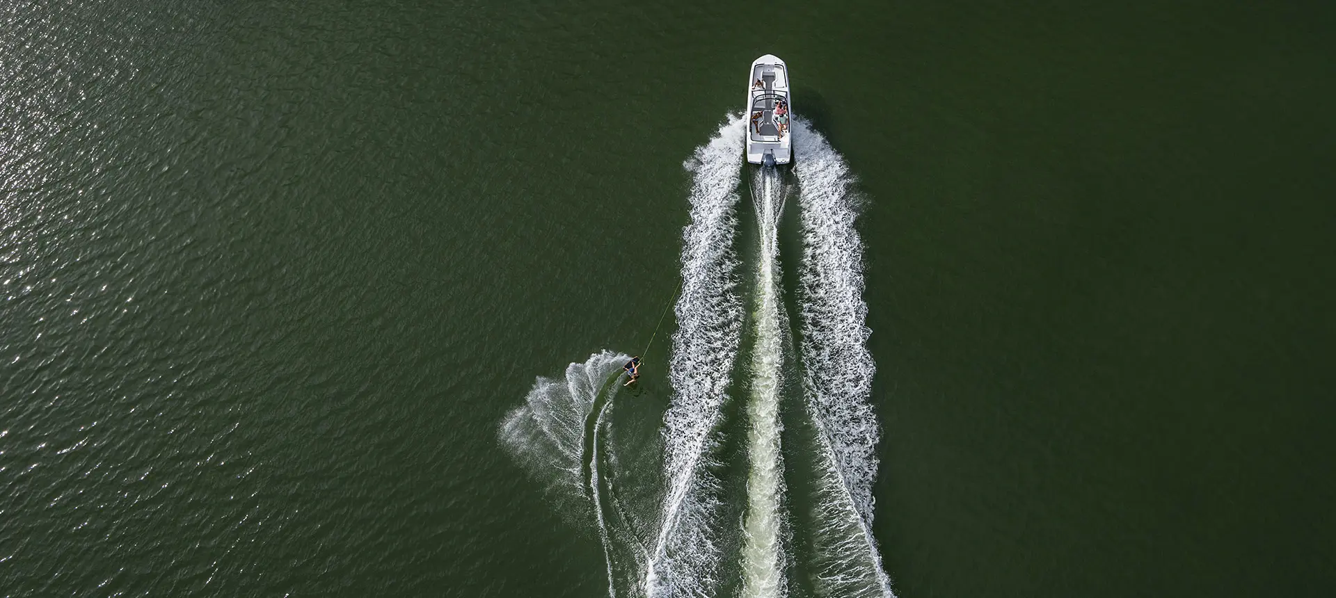 Aerial view of a Hurricane Entertainment deck boat pulling a wakeboarder on a lake.