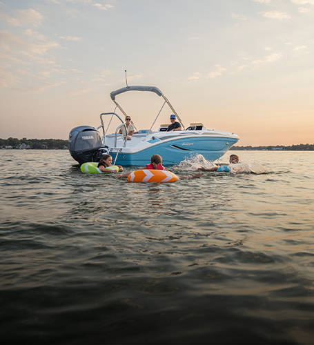 Kids playing in water with floatys near a parked Hurricane Deck Boat. 