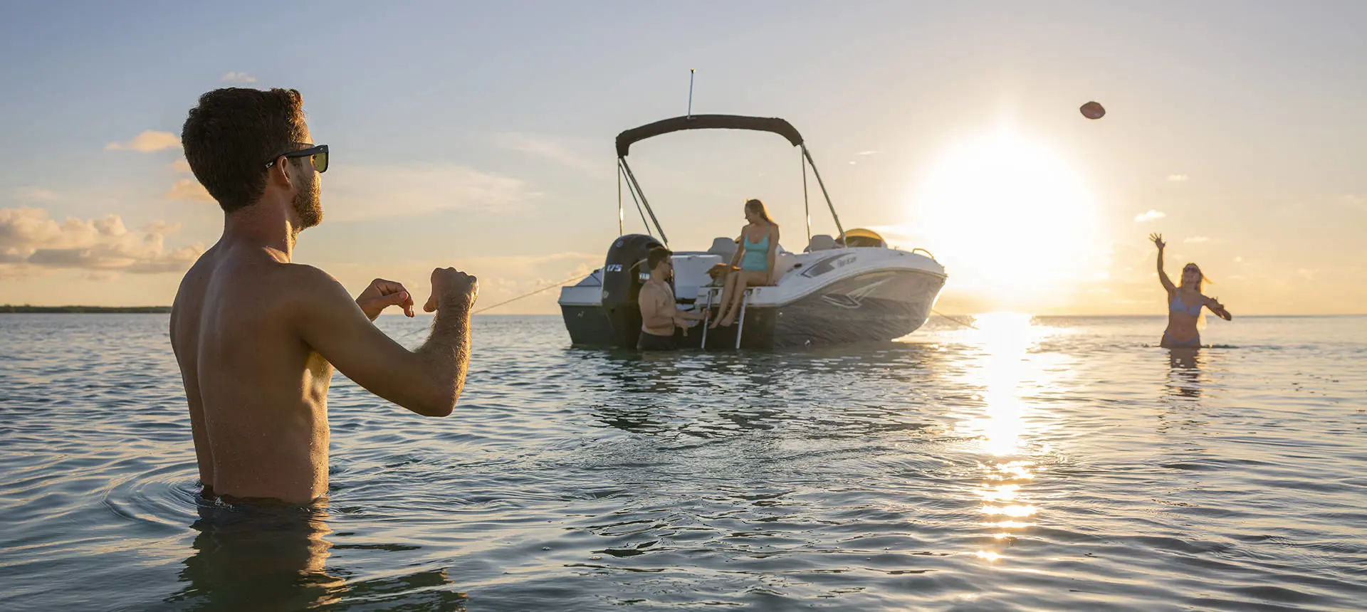 2 people playing catch in the water near a Hurricane SunDeck Sport deck boat.