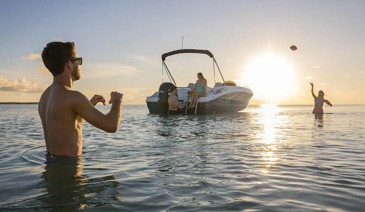 2 people playing catch in the water near a Hurricane SunDeck Sport deck boat.