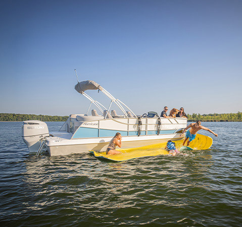 3 children playing on a swimming mat next to a deck boat with an accessory attachment system on the exterior rails