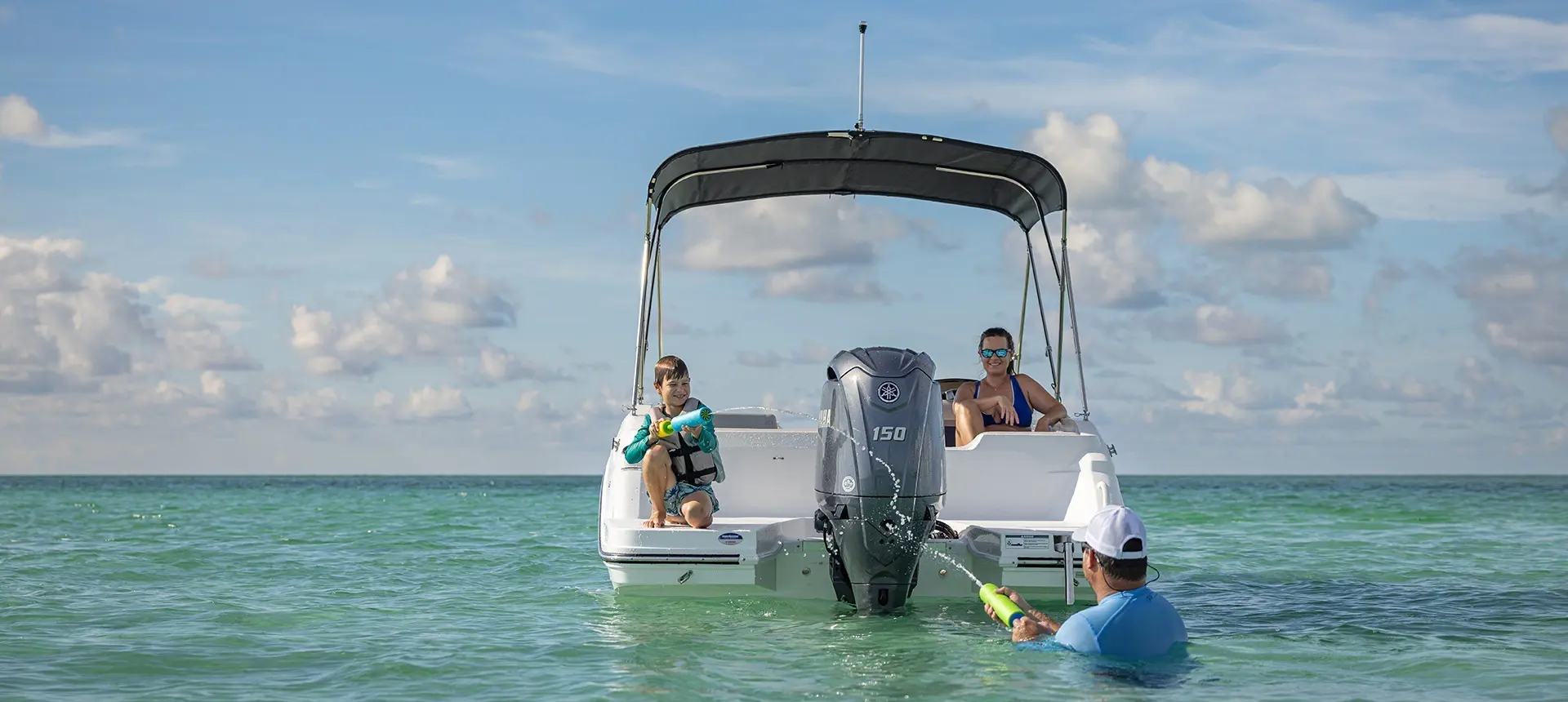 Father and son playing with water toys behind parked a Hurricane Outboard deck boat.
