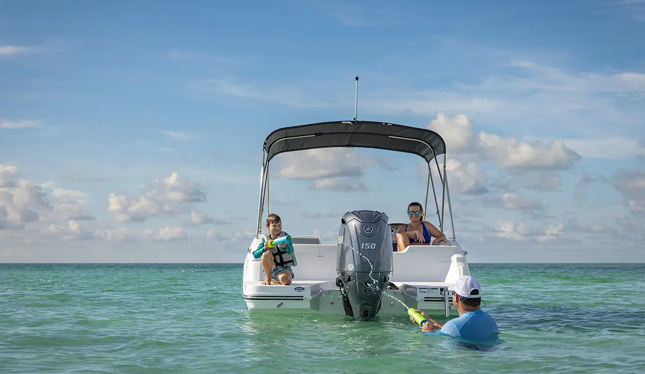 Father and son playing with water toys behind parked a Hurricane Outboard deck boat.