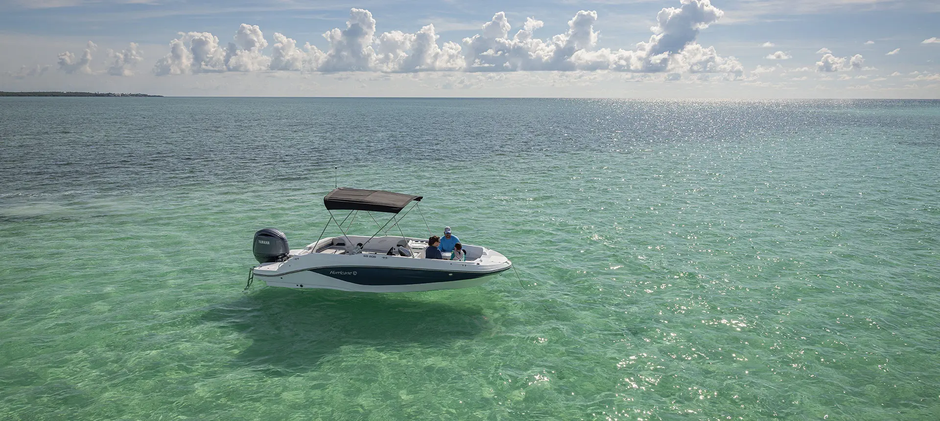 Side view of a Hurricane Outboard deck boat parked on the water.