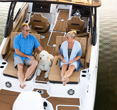 Couple sitting on supportive stern seating with dog on a Hurricane SunDeck 2600 Outboard boat. 
