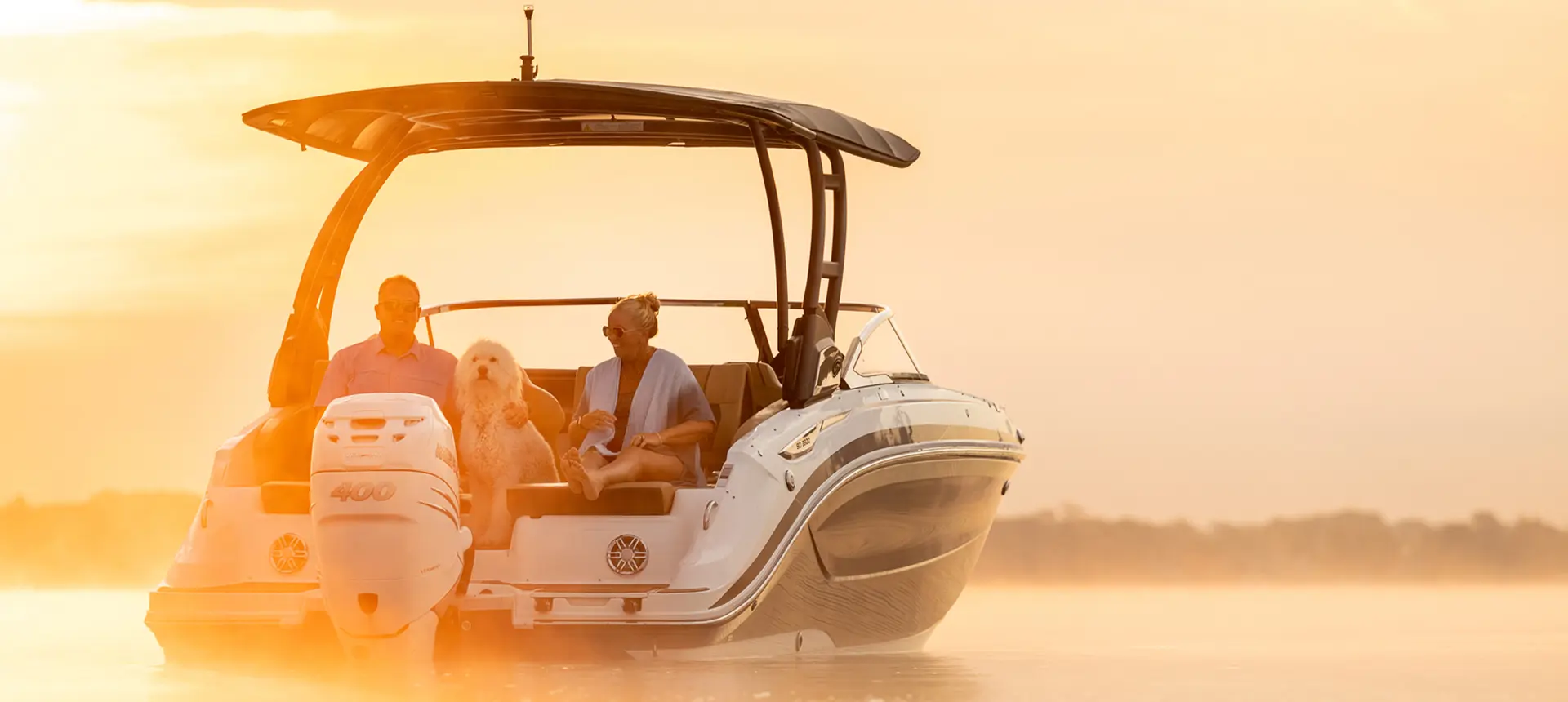 Rear-view of a couple and dog lounging on a parked Hurricane SunDeck 2600 Outboard boat.