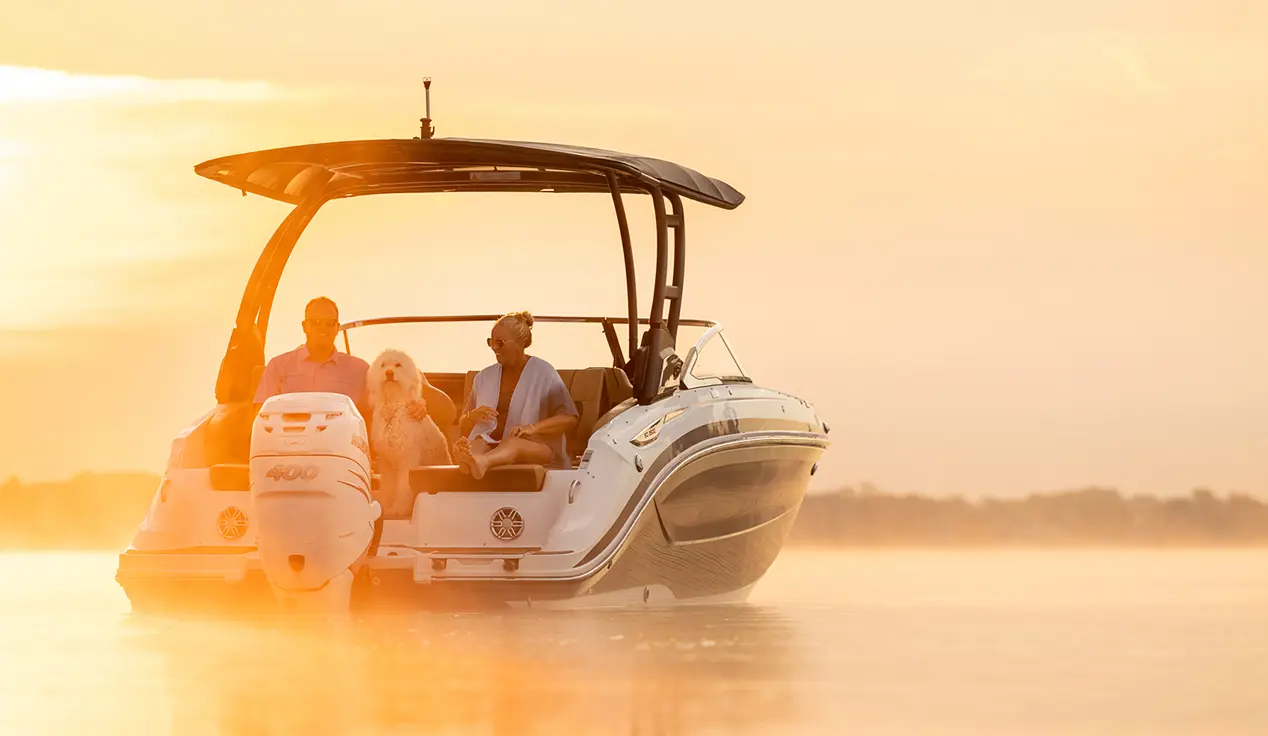 Rear-view of a couple and dog lounging on a parked Hurricane SunDeck 2600 Outboard boat.