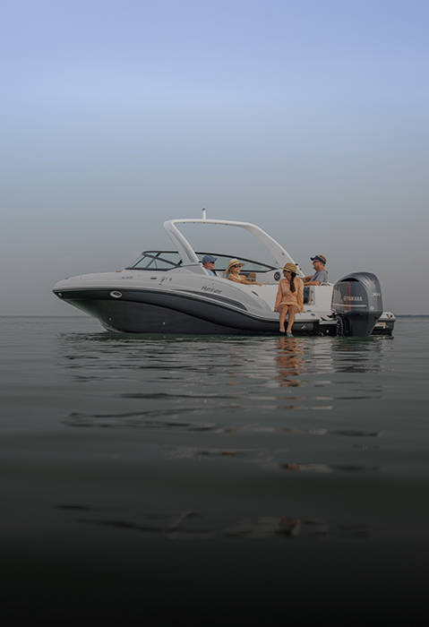 Side view of a parked Hurricane SunDeck 2690 Outboard boat with a group of friends lounging. 
