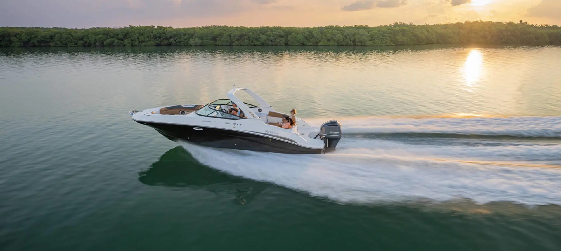 Side view of a Hurricane SunDeck 2690 Outboard boat at sunset.