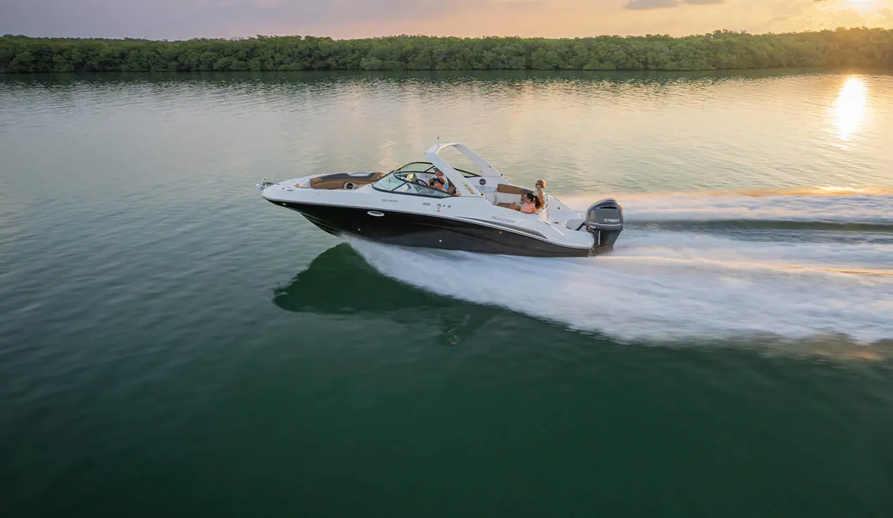 Side view of a Hurricane SunDeck 2690 Outboard boat at sunset.