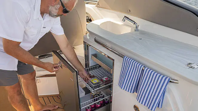 Man removing fruit out of fridge storage on a Hurricane 3200 Outboard boat.