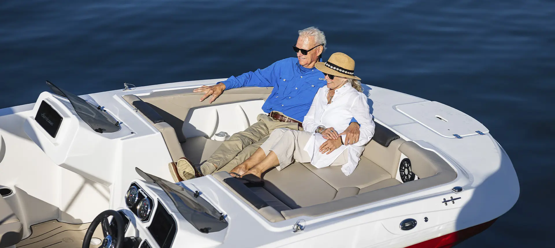 Man and woman lounging in front seating of a parked Hurricane SunDeck Sport boat.