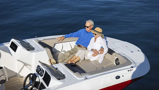 Man and woman lounging in front seating of a parked Hurricane SunDeck Sport boat.