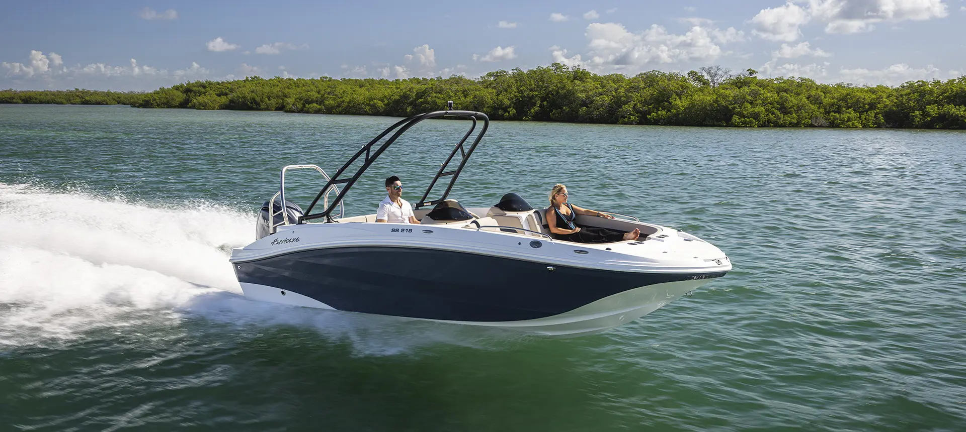 Couple speeding across blue water on a Hurricane SunDeck Sport boat.