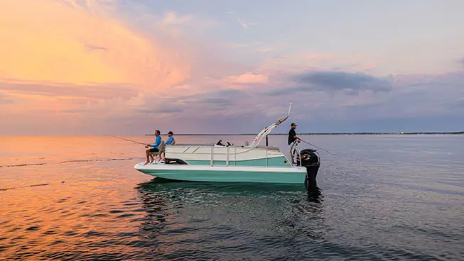 3 people fishing on a Hurricane fishing boat at sunset.