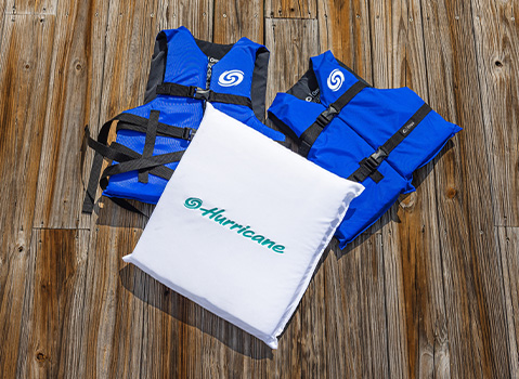 Hurricane‑branded blue Coast Guard–approved life jackets and a white throwable flotation cushion displayed on a dock.