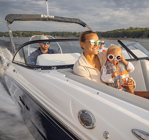 A woman holding a child while relaxing comfortably on the bow seats of a Hurricane deck boat.