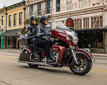 two people riding an Indian Motorcycle on a street in the city