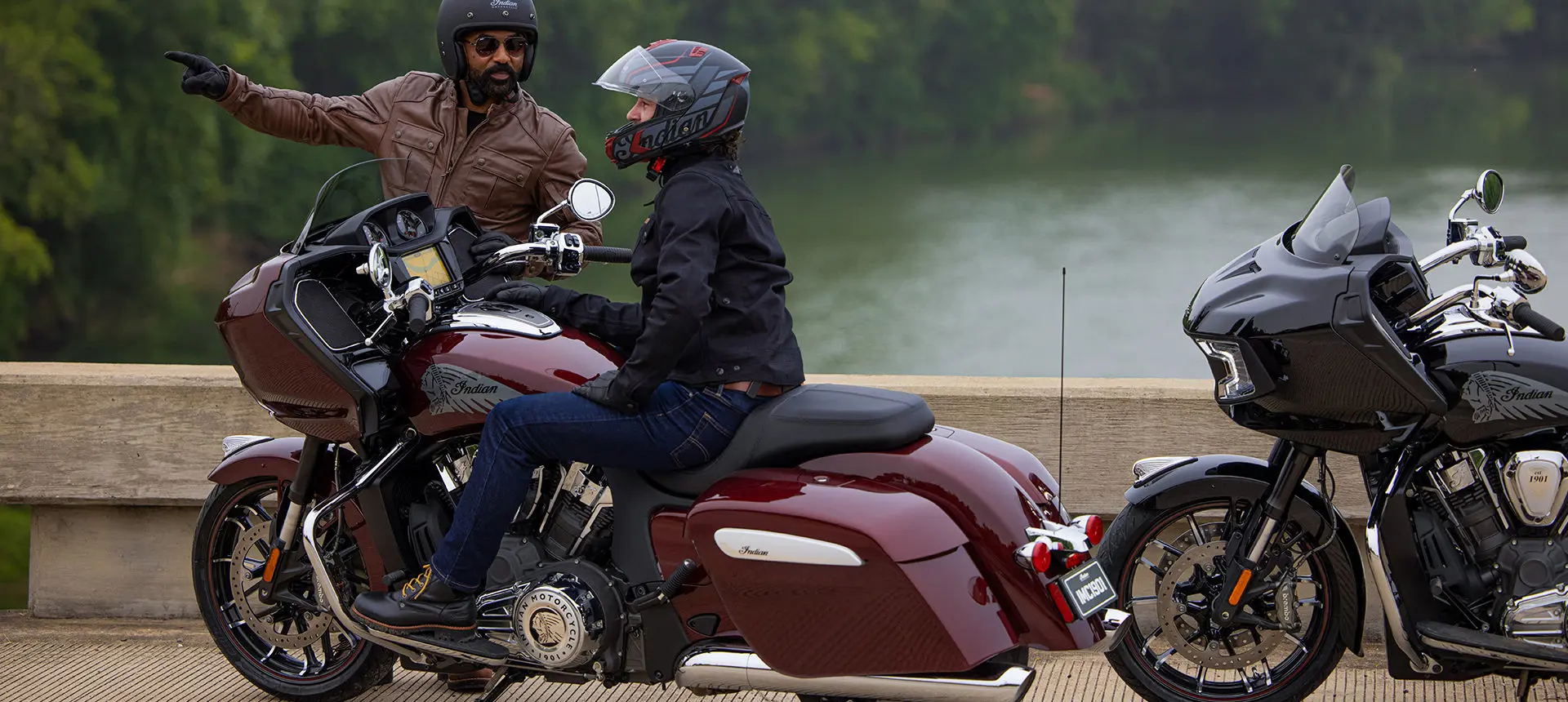person sitting on a maroon metallic indian challenger limited motorcycle while a man nearby provides direction