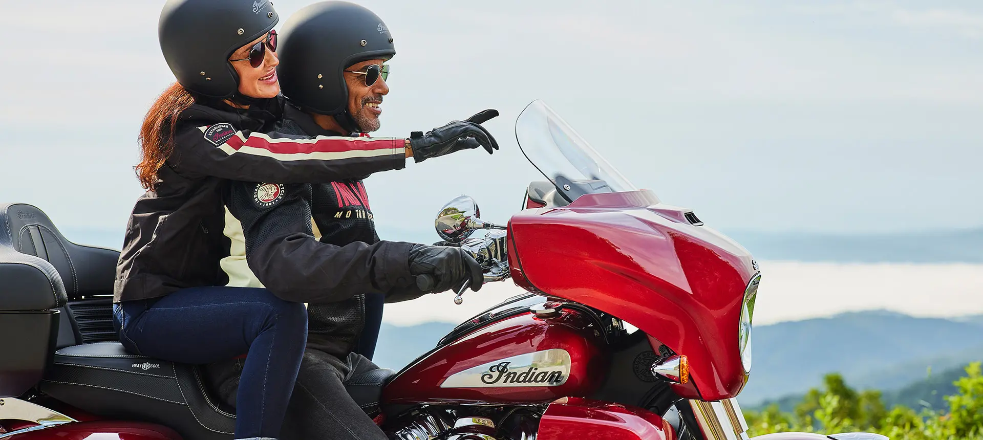 woman pointing ahead while a man holds onto the handlebars of an indian roadmaster limited motorcycle