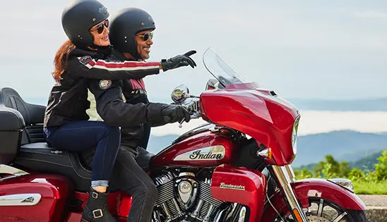 woman pointing ahead while a man holds onto the handlebars of an indian roadmaster limited motorcycle