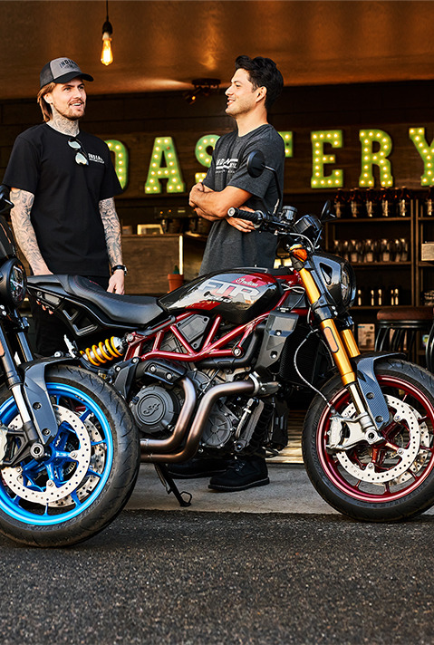 2 men chatting near their Indian FTR motorcycles.