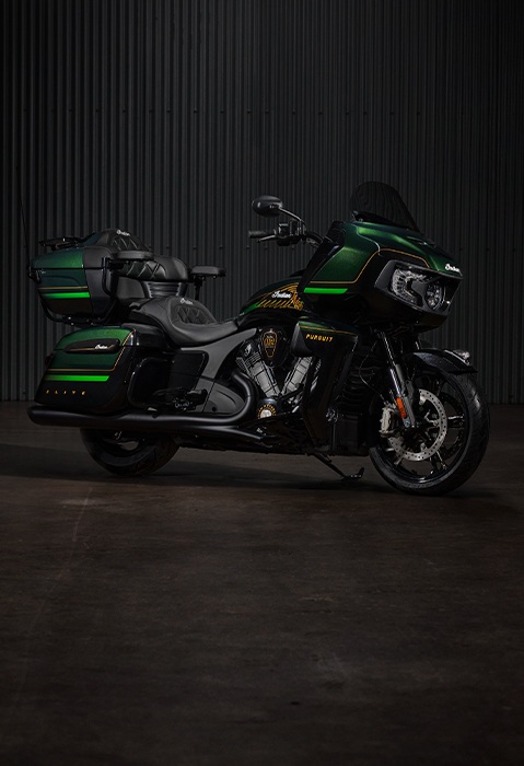 Perfil lateral de una motocicleta touring Indian Pursuit Elite de 2025 estacionada en una cochera oscura.