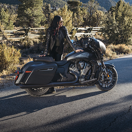 A woman standing near an Indian Bagger motorcycle showcasing the saddlebags and storage options. 