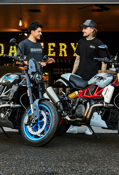 2 men chatting behind their Indian FTR standard-style motorcycles.