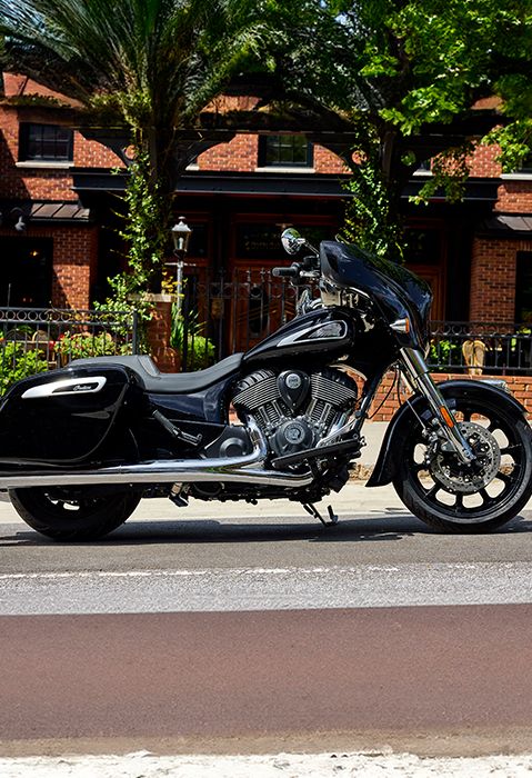 Side profile of a 2025 Indian Chieftain bagger motorcycle parked in front of a brick building.